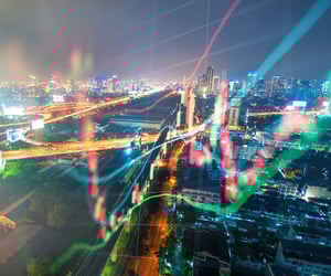 Night view of a city overlaid with financial or stock data in the form of line and candlestick charts.